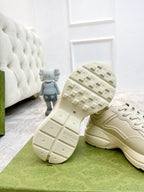 Unisex sneaker with visible treaded outsole, light color upper with red logo patch.
