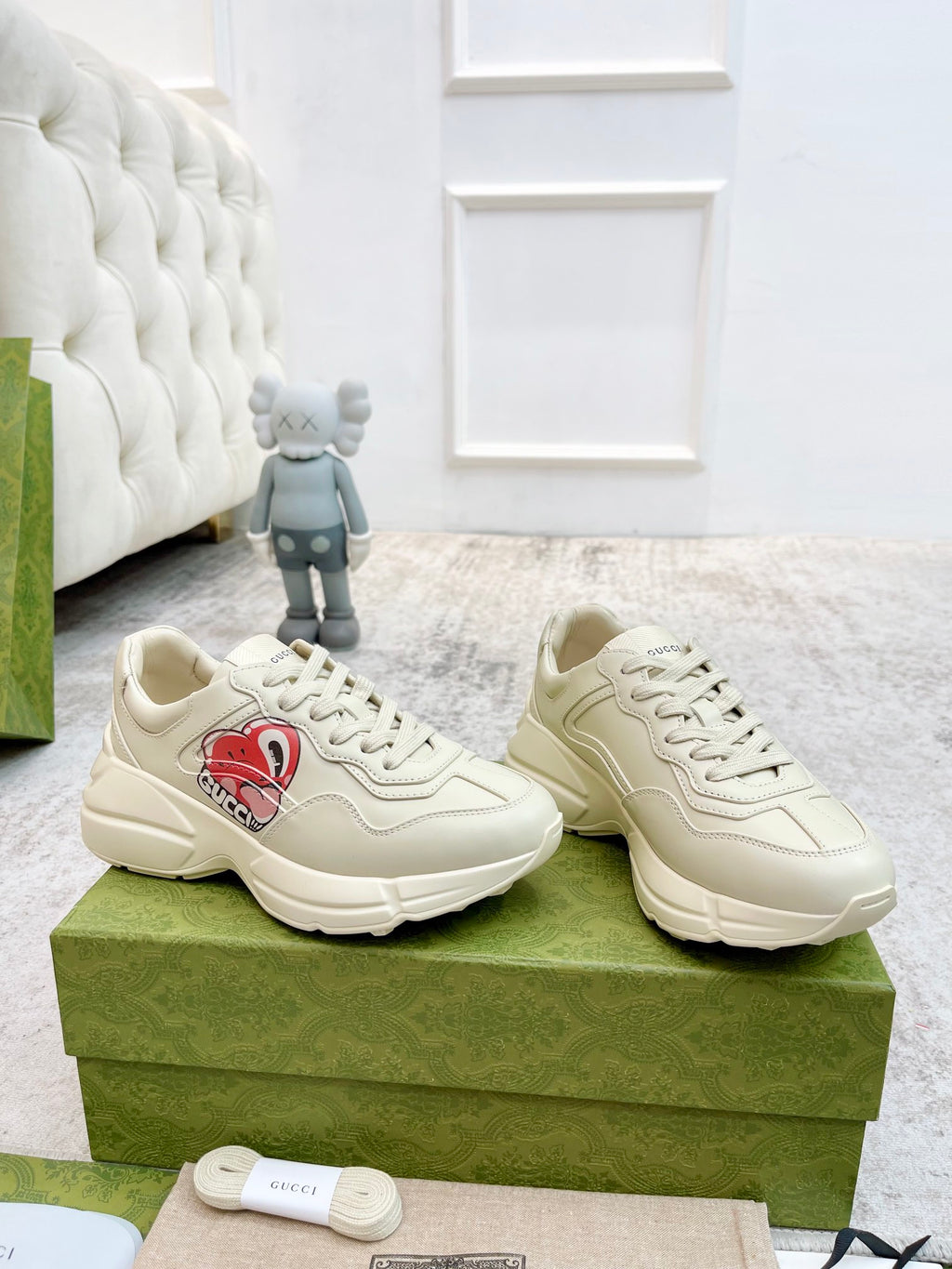 Pair of unisex low-top sneakers in light color with red logo patch, lace-up front view.