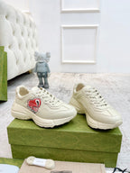 Pair of unisex low-top sneakers in light color with red logo patch, lace-up front view.