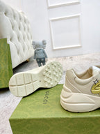 Cream sneaker outsole with tread and stitched logos; side view on green box