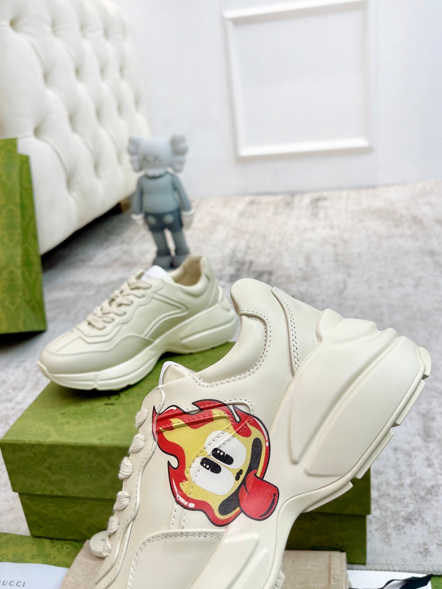 Cream lace-up sneakers with red cartoon face patch on side and rounded toe