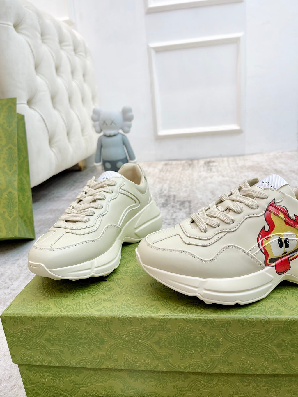 Cream lace-up sneakers with cartoon patch; two shoes on green display box