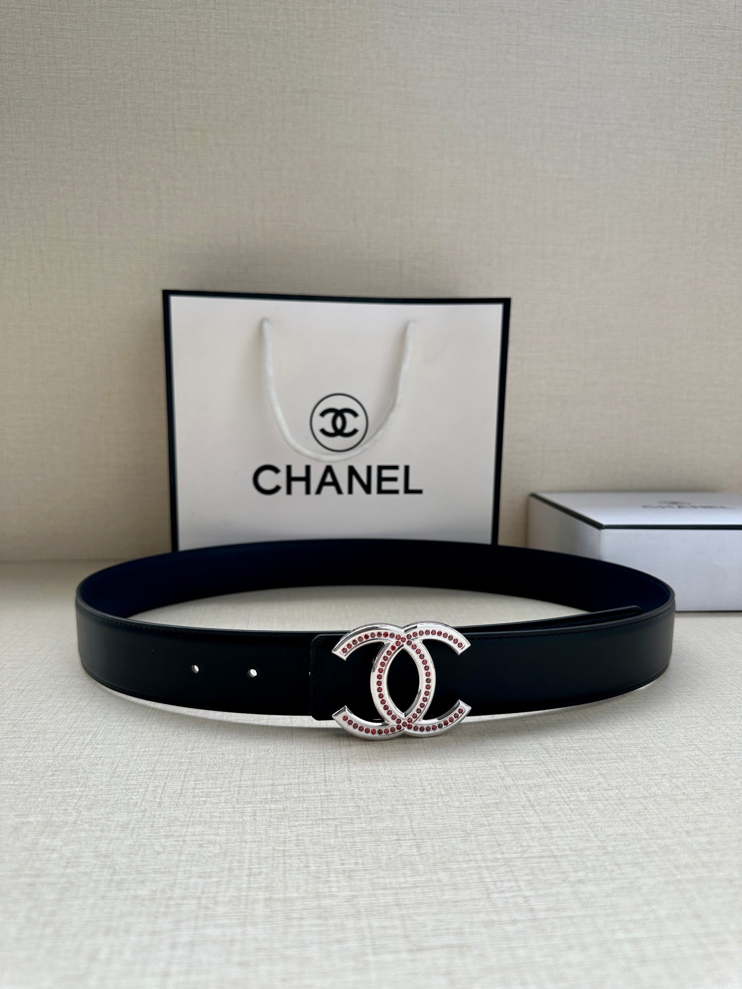Dark leather belt with CC-style buckle and pink stone accents on display