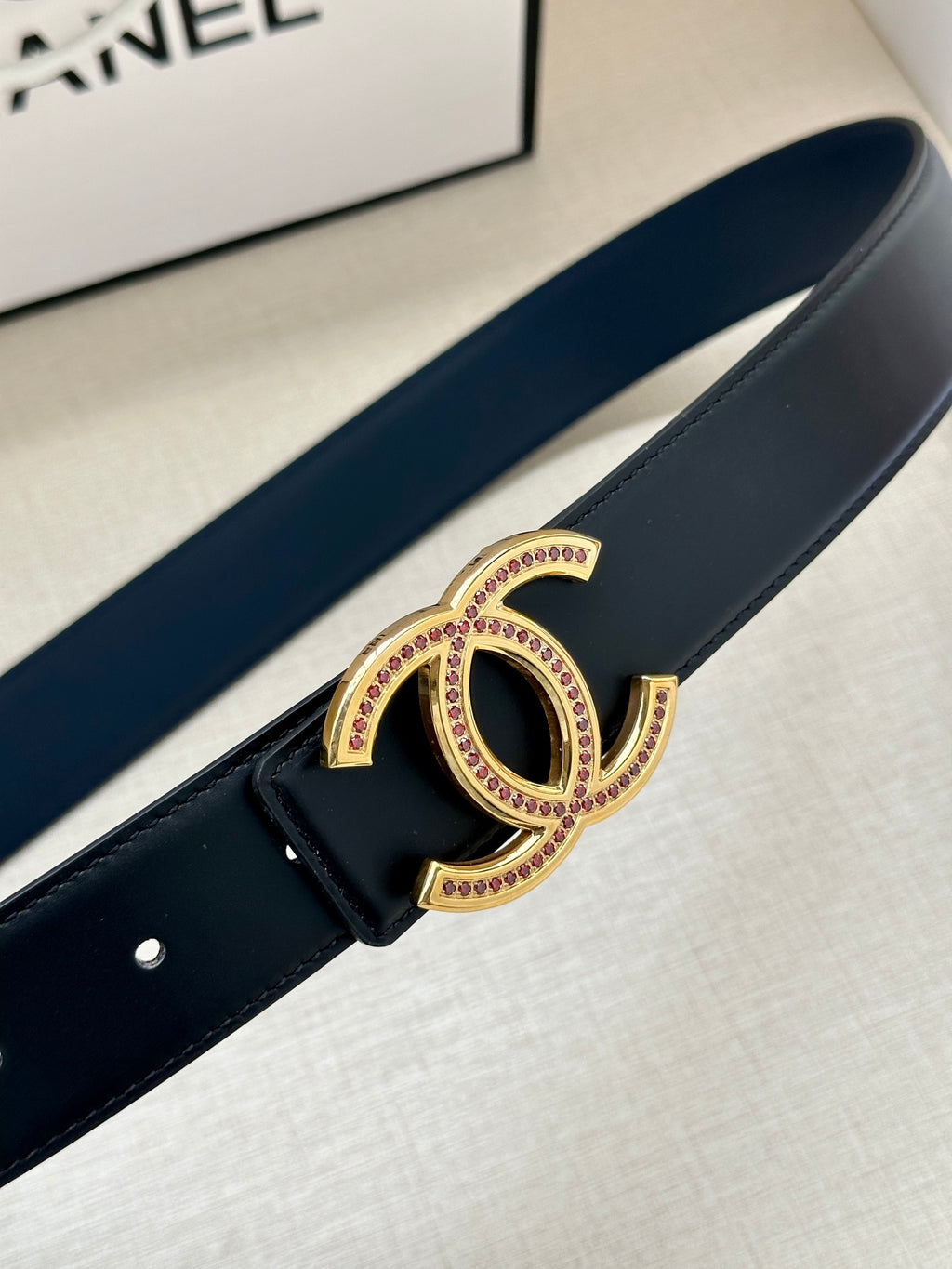 Dark leather belt close-up with gold CC-style buckle and pink stone trim