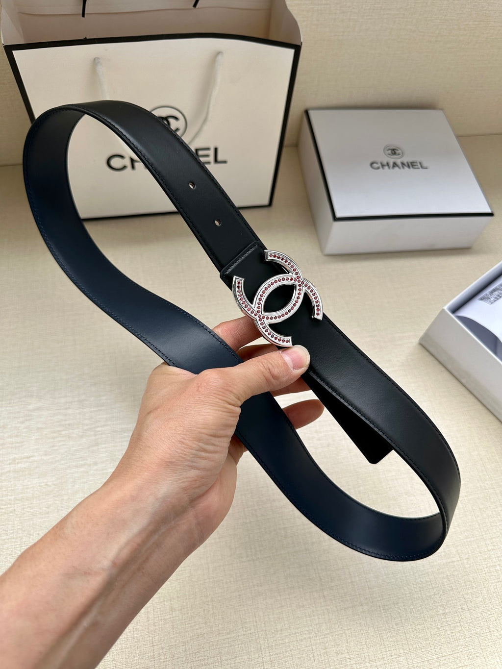 Dark leather belt looped in hand, showing CC-style buckle with stone inlays