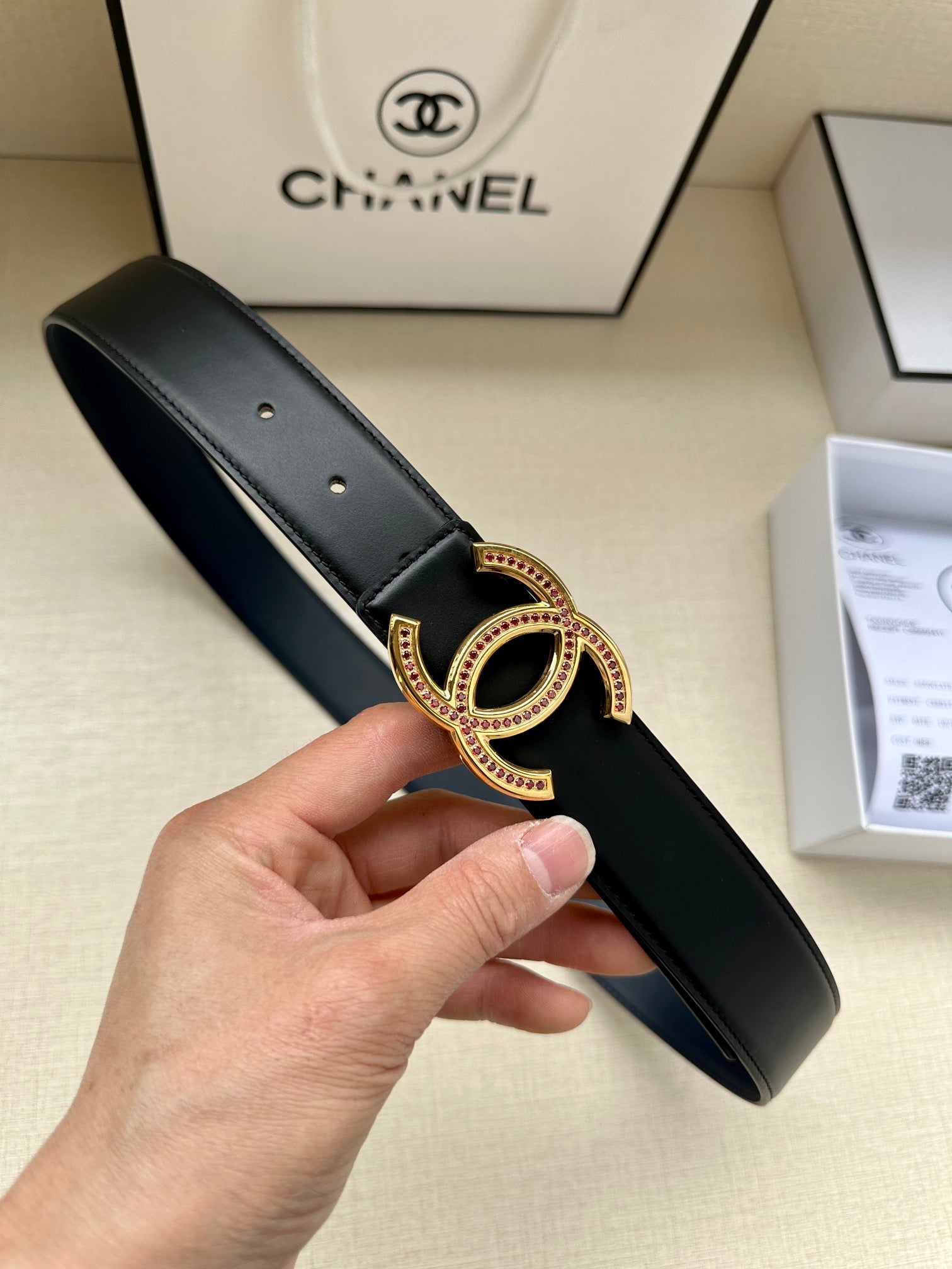 Dark leather belt with gold CC-style buckle and pink stone accents, held in hand