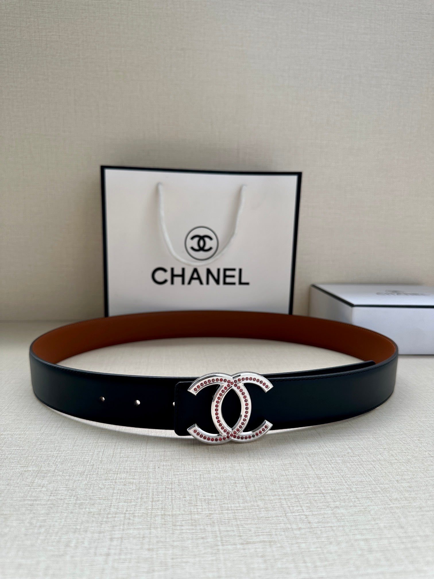 Black leather belt with central jeweled double-C buckle on a wide strap.