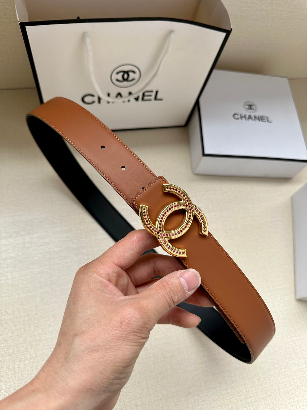 Brown leather belt with small holes and gold-tone double-C buckle.