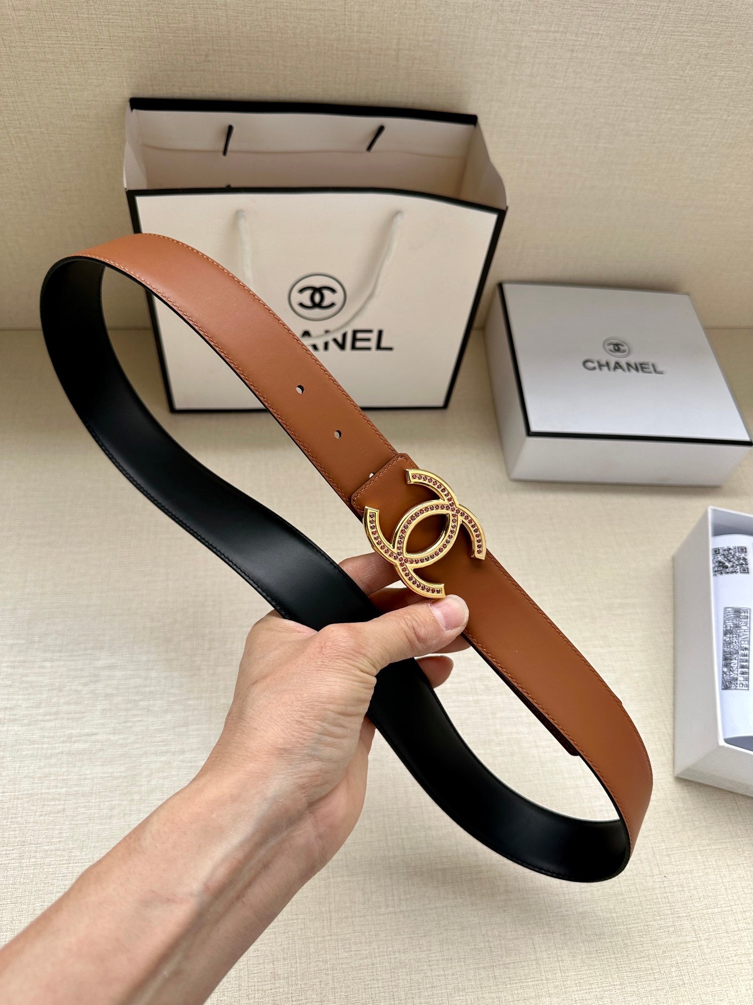 Brown leather belt with gold-tone double-C buckle and pierced holes.