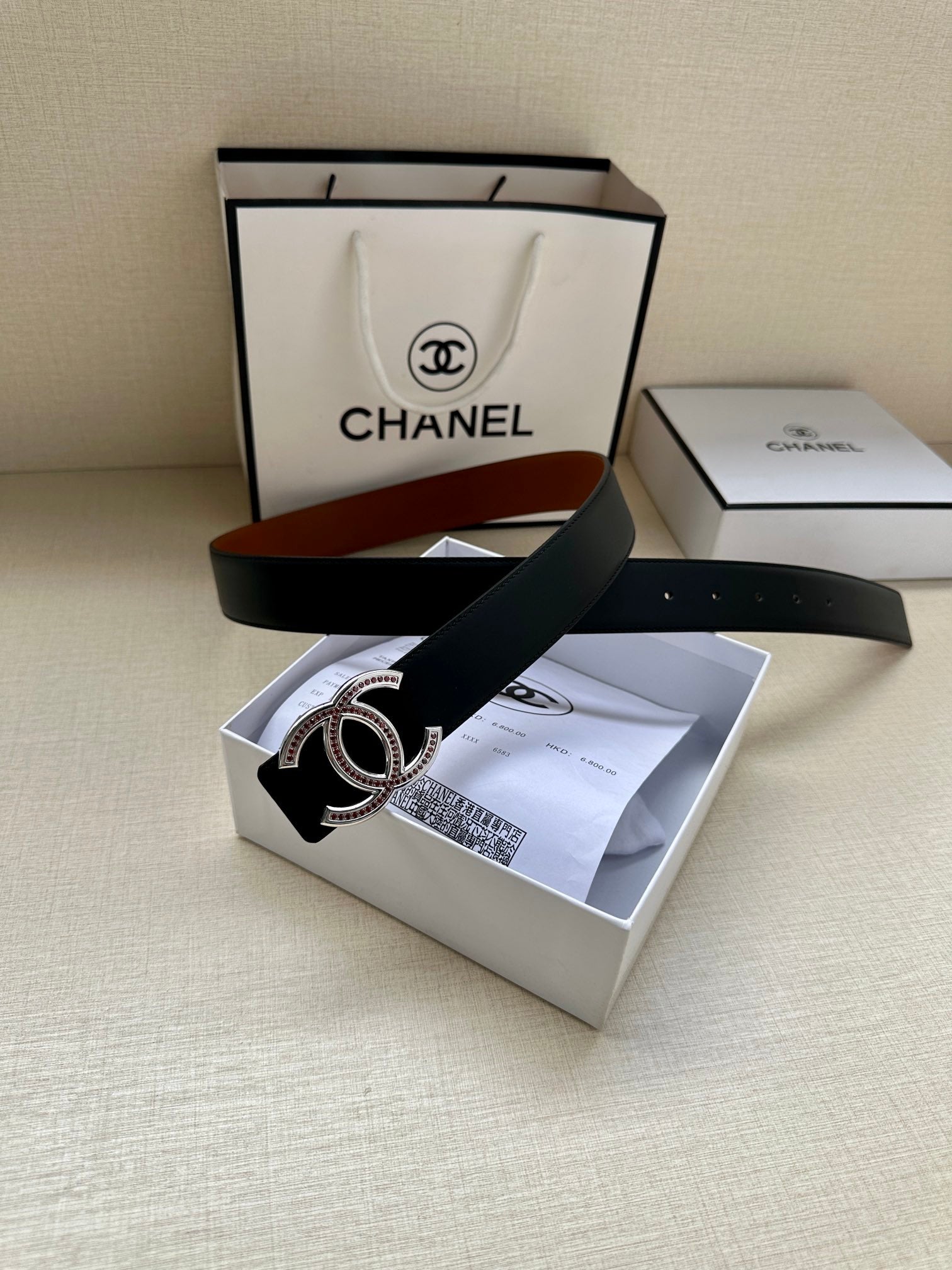 Black leather belt with double-C buckle and jeweled accents, laid on box.