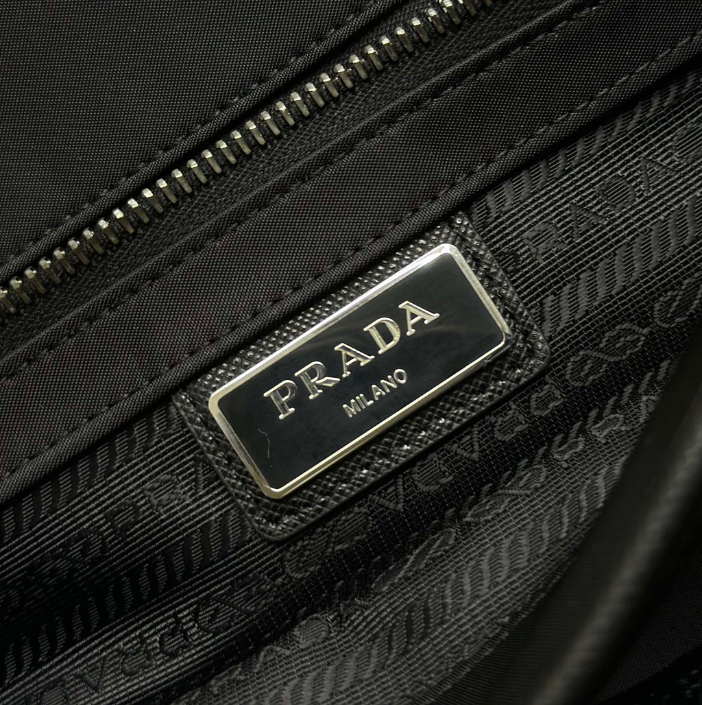 Prada bag detail with silver logo plaque and textured zip area on dark fabric