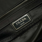 Prada bag detail with silver logo plaque and textured zip area on dark fabric