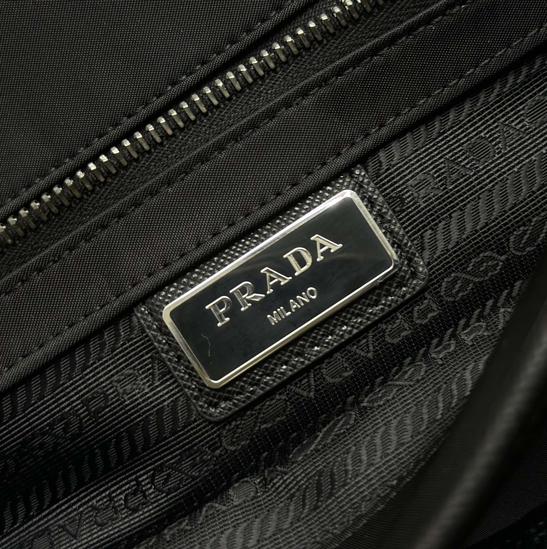 Prada logo plaque on black textured bag with zip closure, black