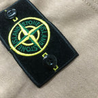 Stone Island black logo patch with yellow emblem on beige shorts
