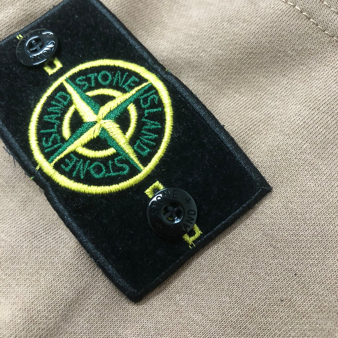 Stone Island black logo patch with yellow emblem on beige shorts