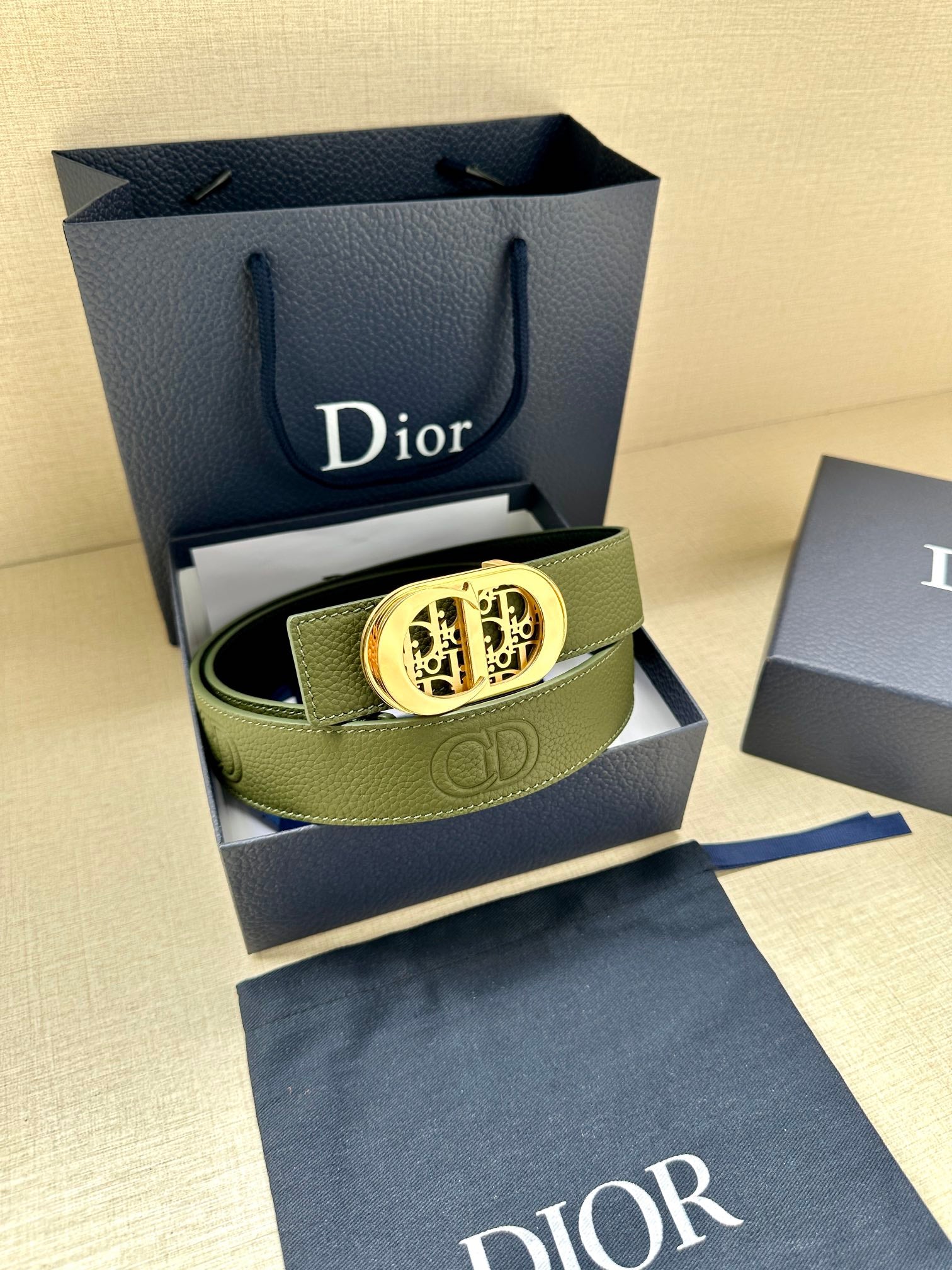 Green leather belt with gold-toned oval logo buckle and textured leather surface