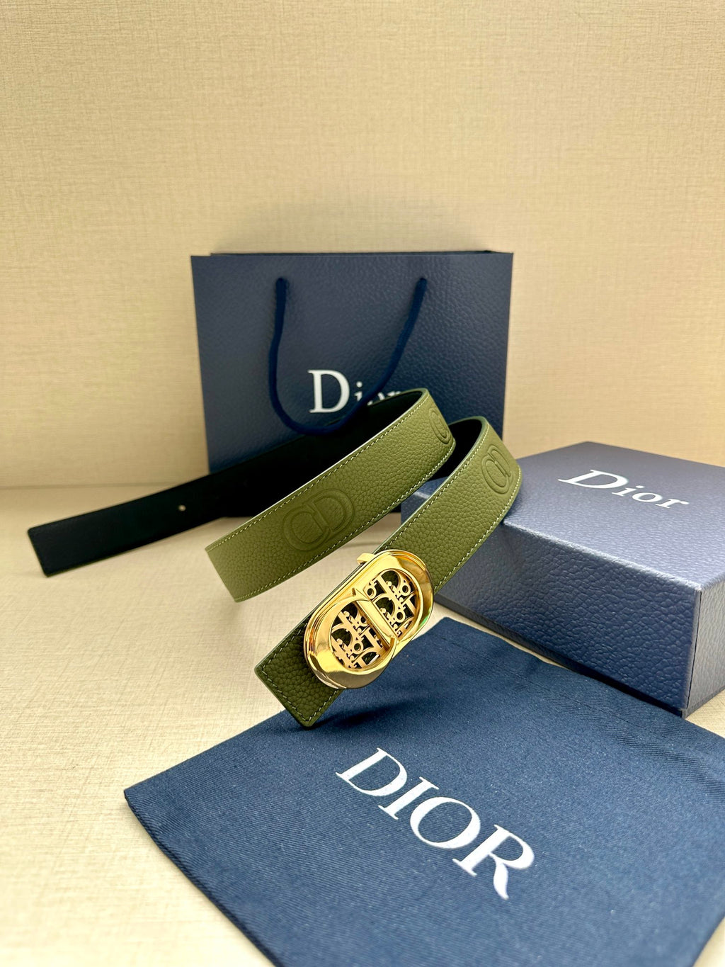Green leather belt with gold-toned oval logo buckle and embossed monogram