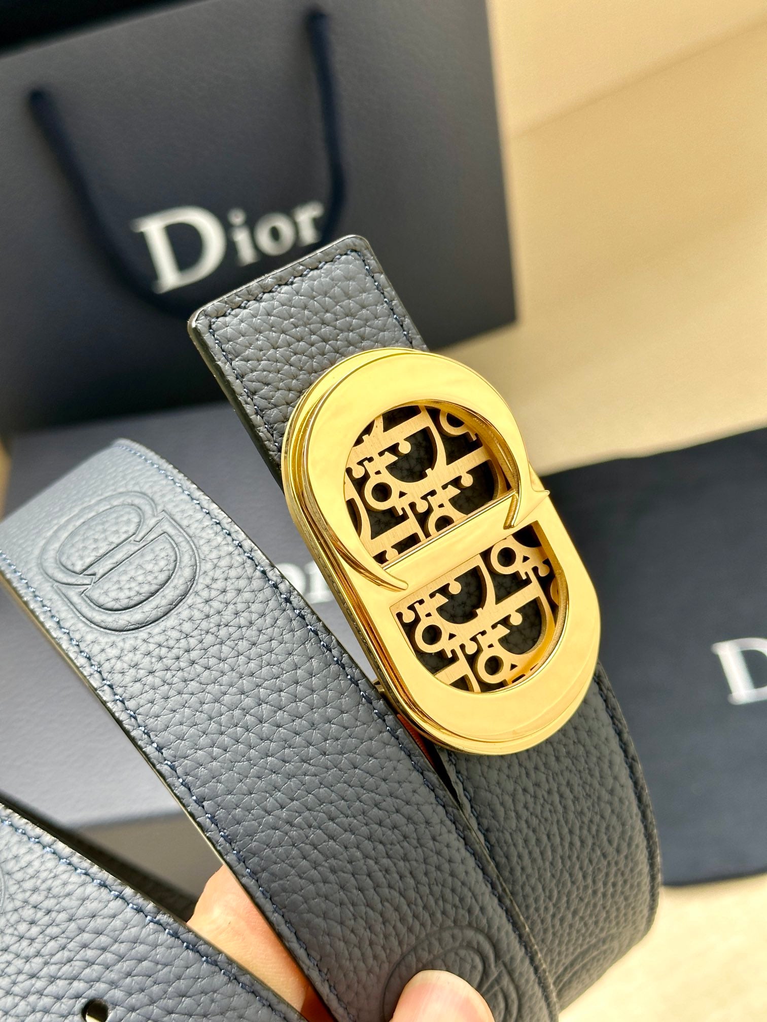 Dior leather belt detail: textured dark blue strap with gold-tone logo buckle