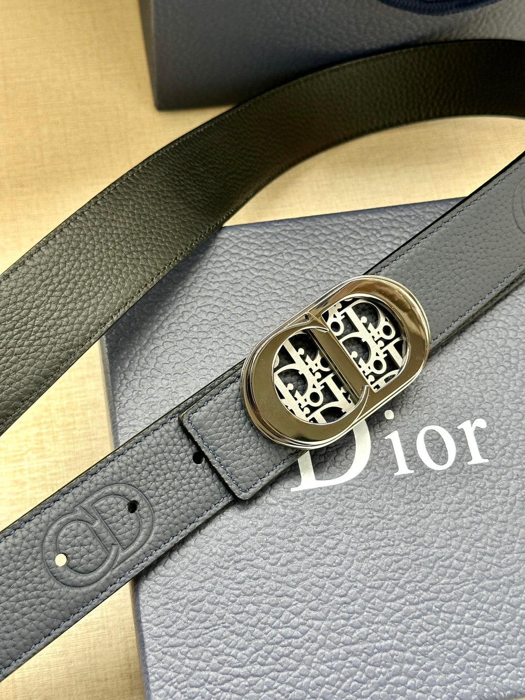 Dior leather belt close-up: textured dark blue strap and gold-tone logo buckle