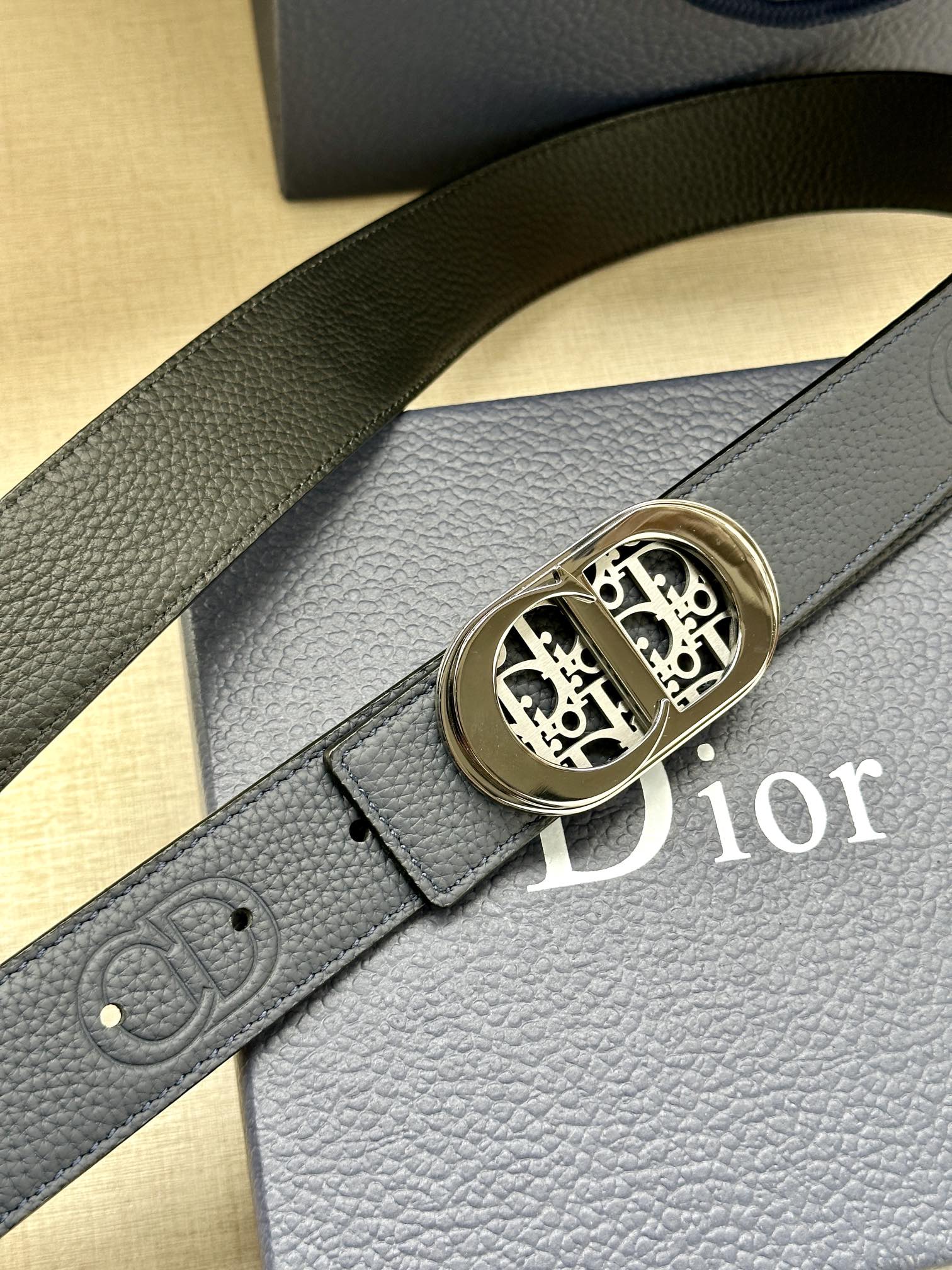 Dior leather belt close-up: textured dark blue strap and gold-tone logo buckle