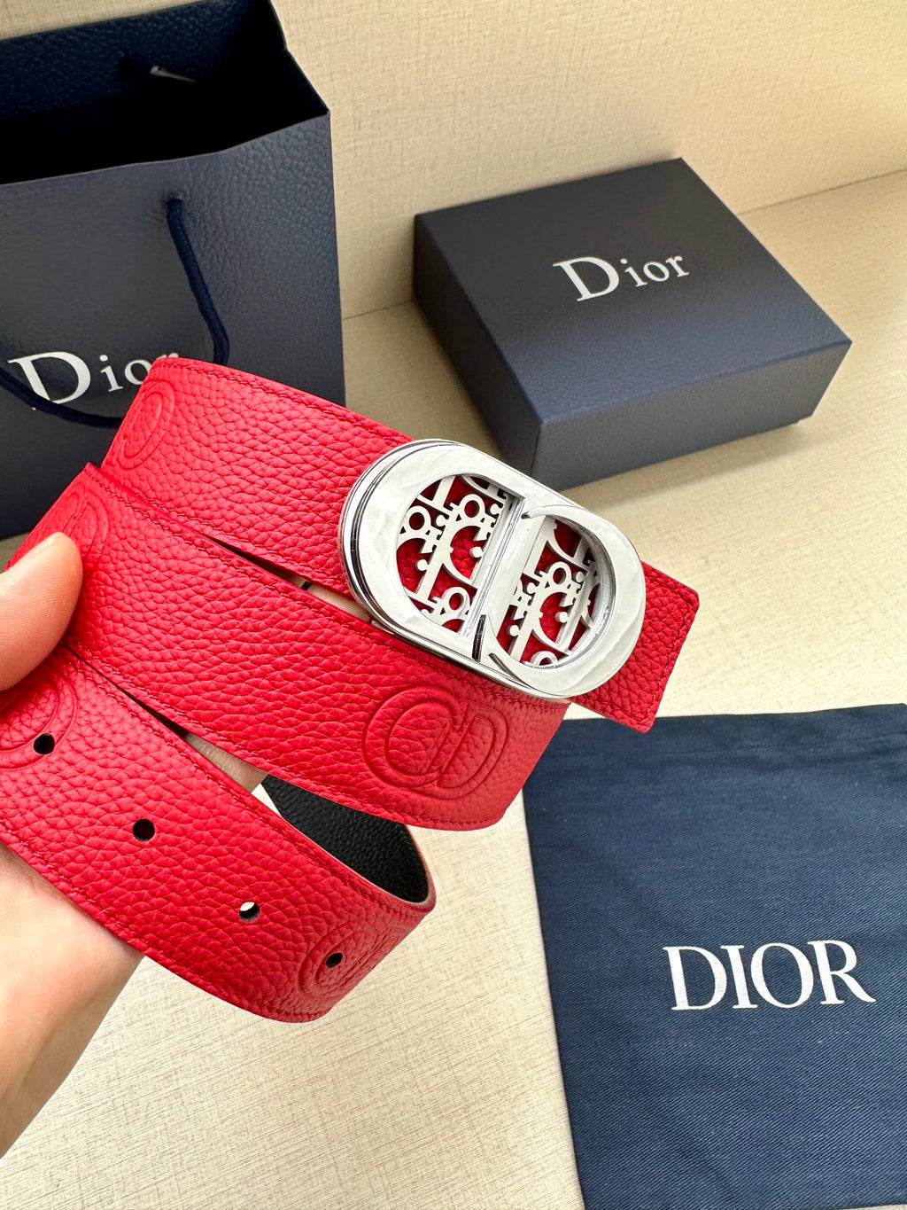 Red leather belt with silver-tone oval logo buckle and perforated hole line