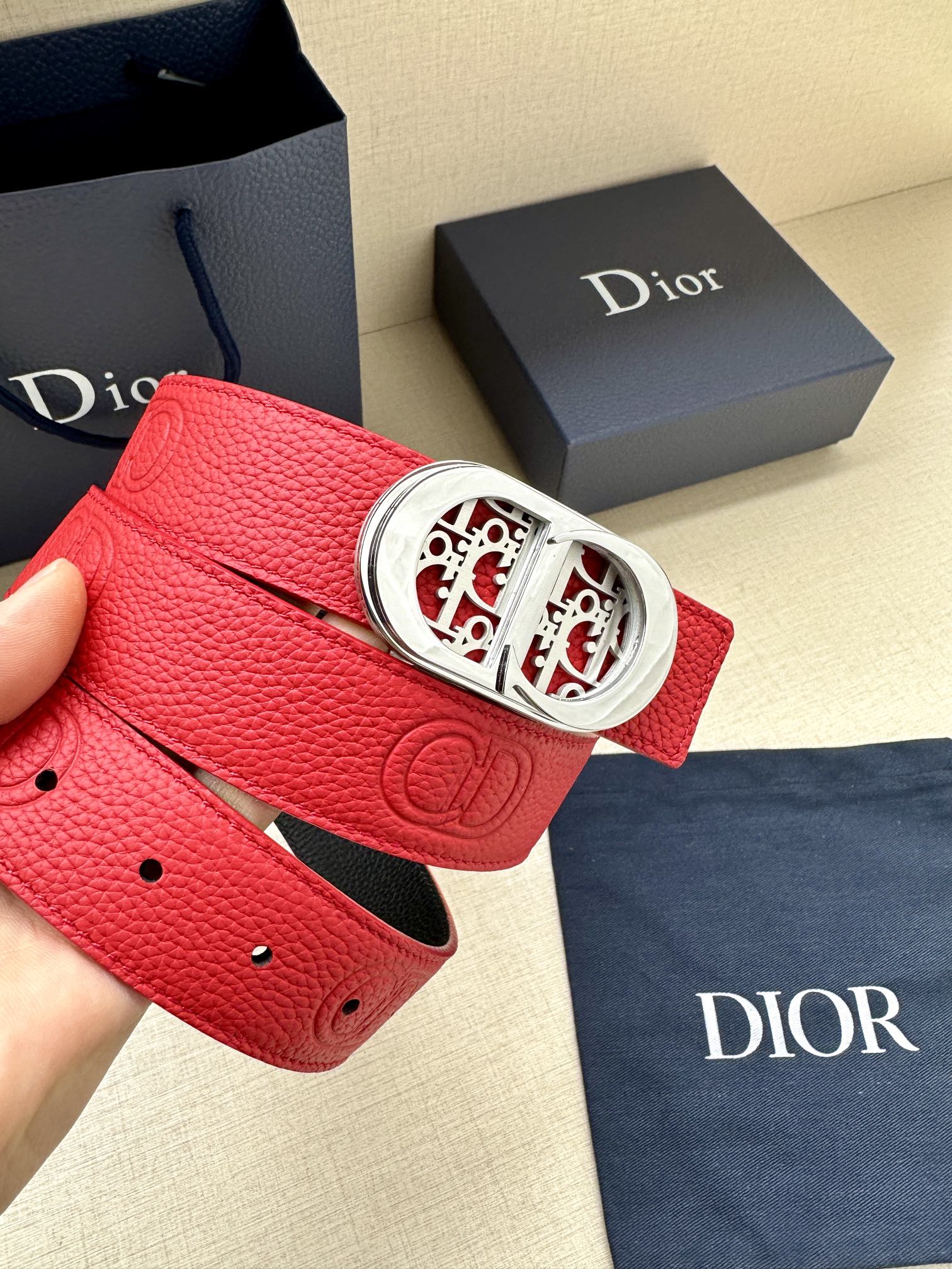 Red leather belt with silver-tone oval logo buckle and perforated hole line