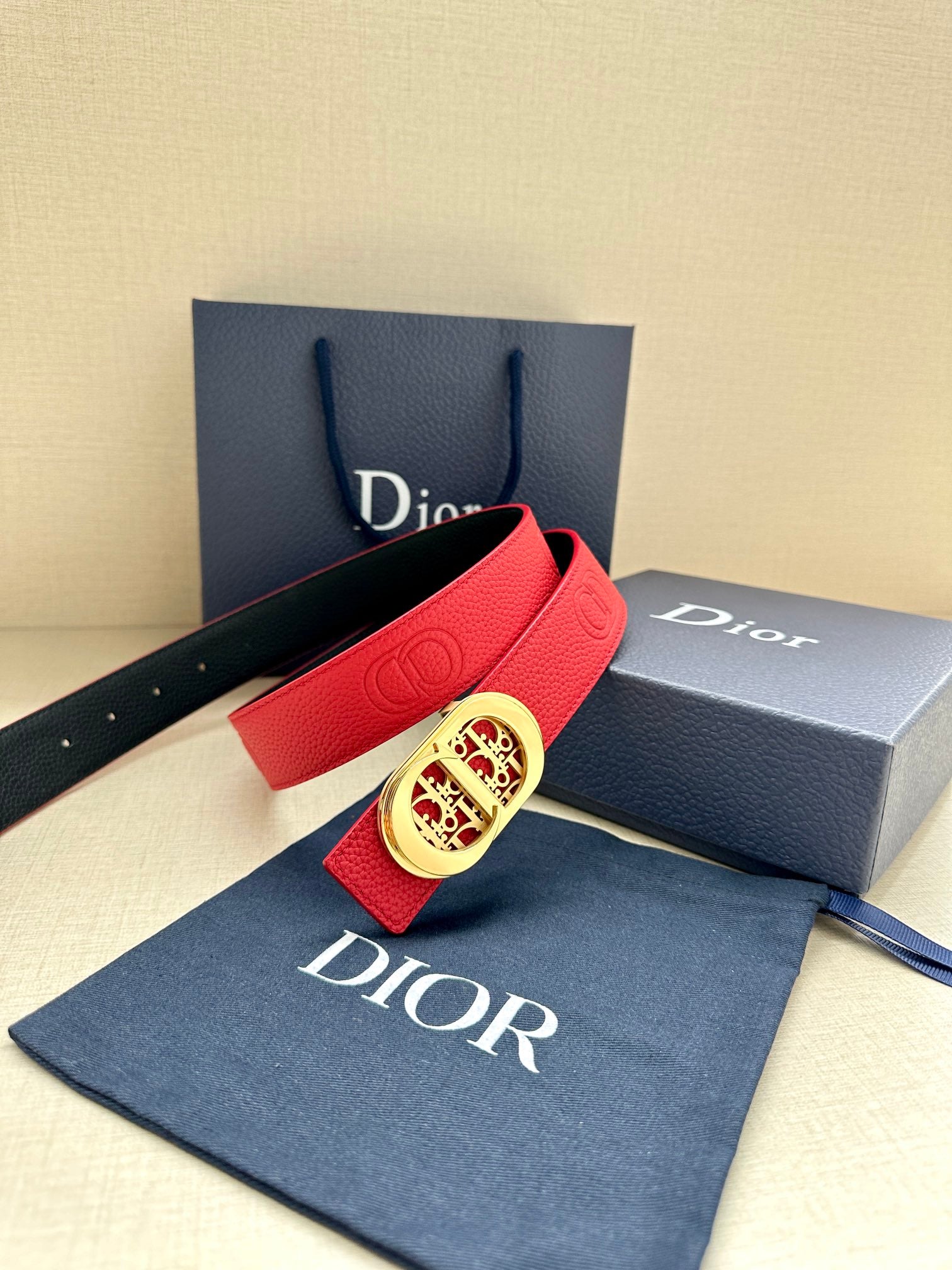Red leather belt with gold-tone oval logo buckle and embossed strap panel