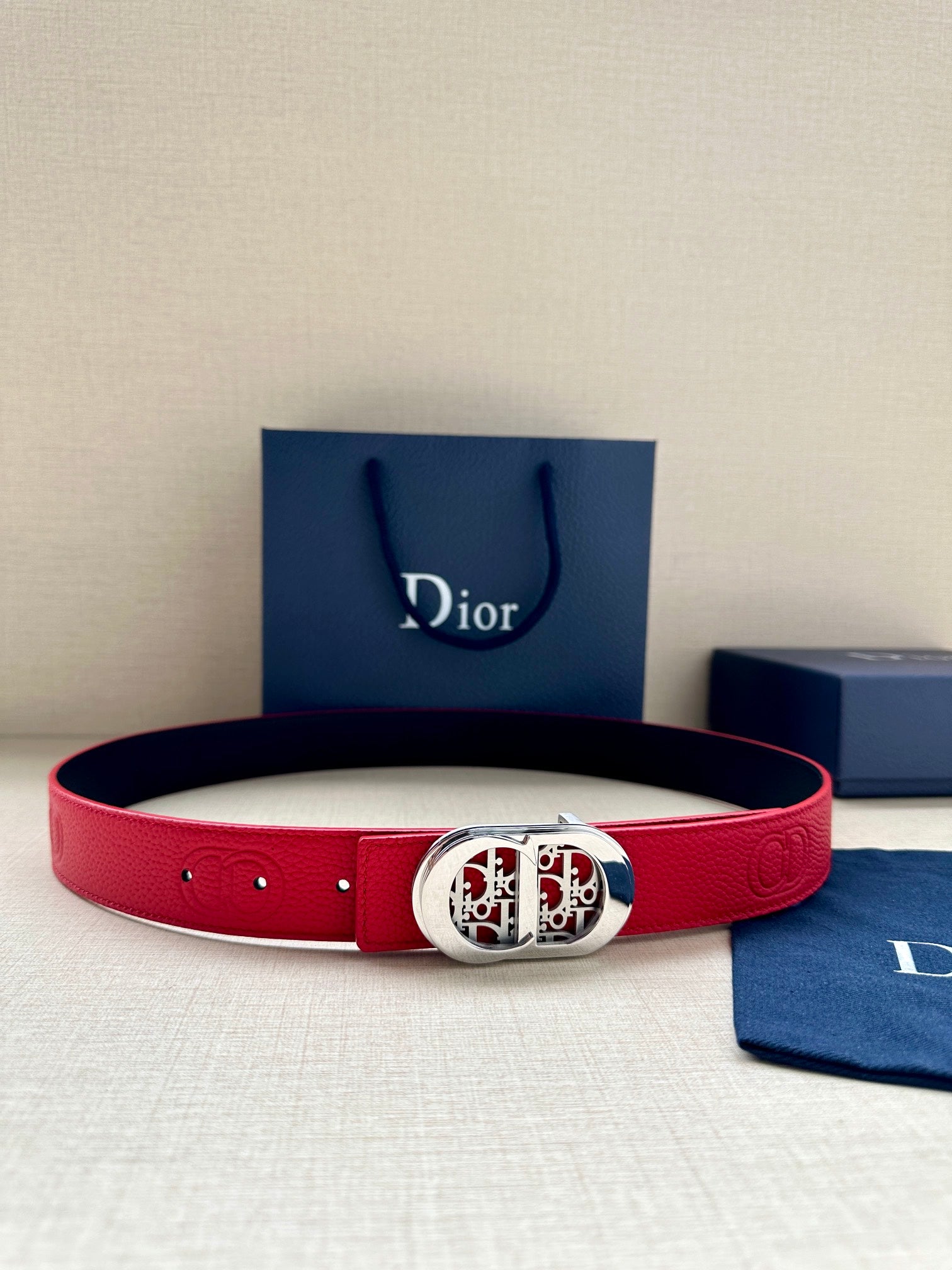 Red leather belt with silver-tone oval logo buckle and round grommet holes