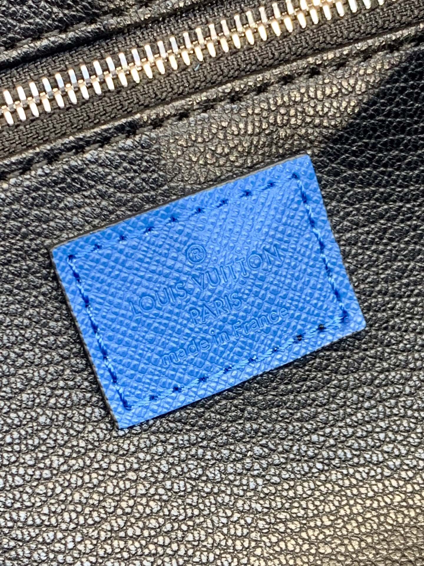 Louis Vuitton blue monogram leather patch detail on dark zipper