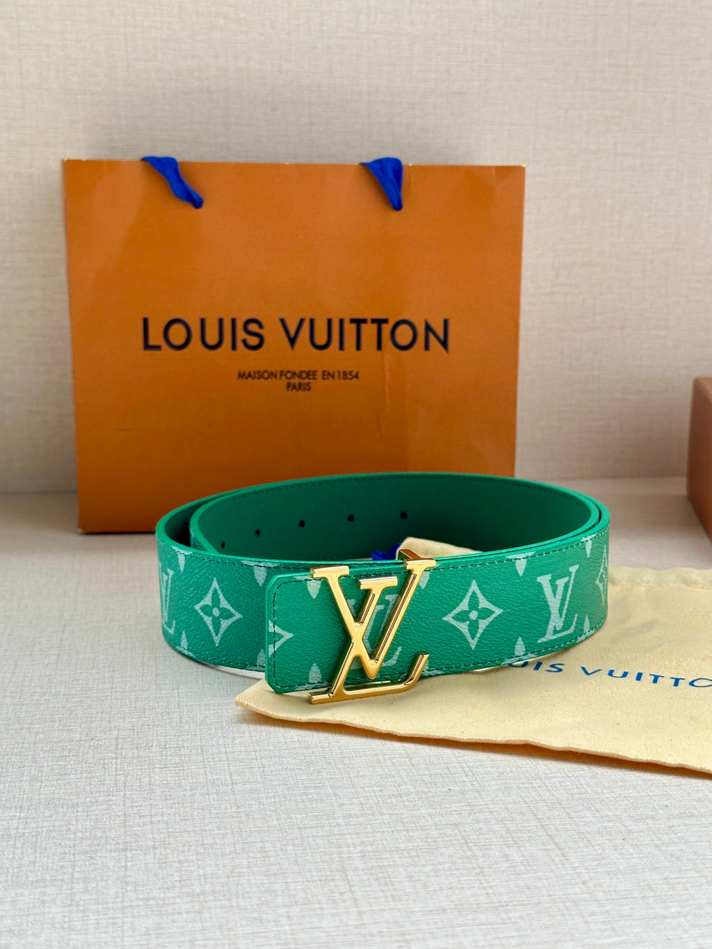 Louis Vuitton green monogram belt with LV gold buckle, shown near dust bag