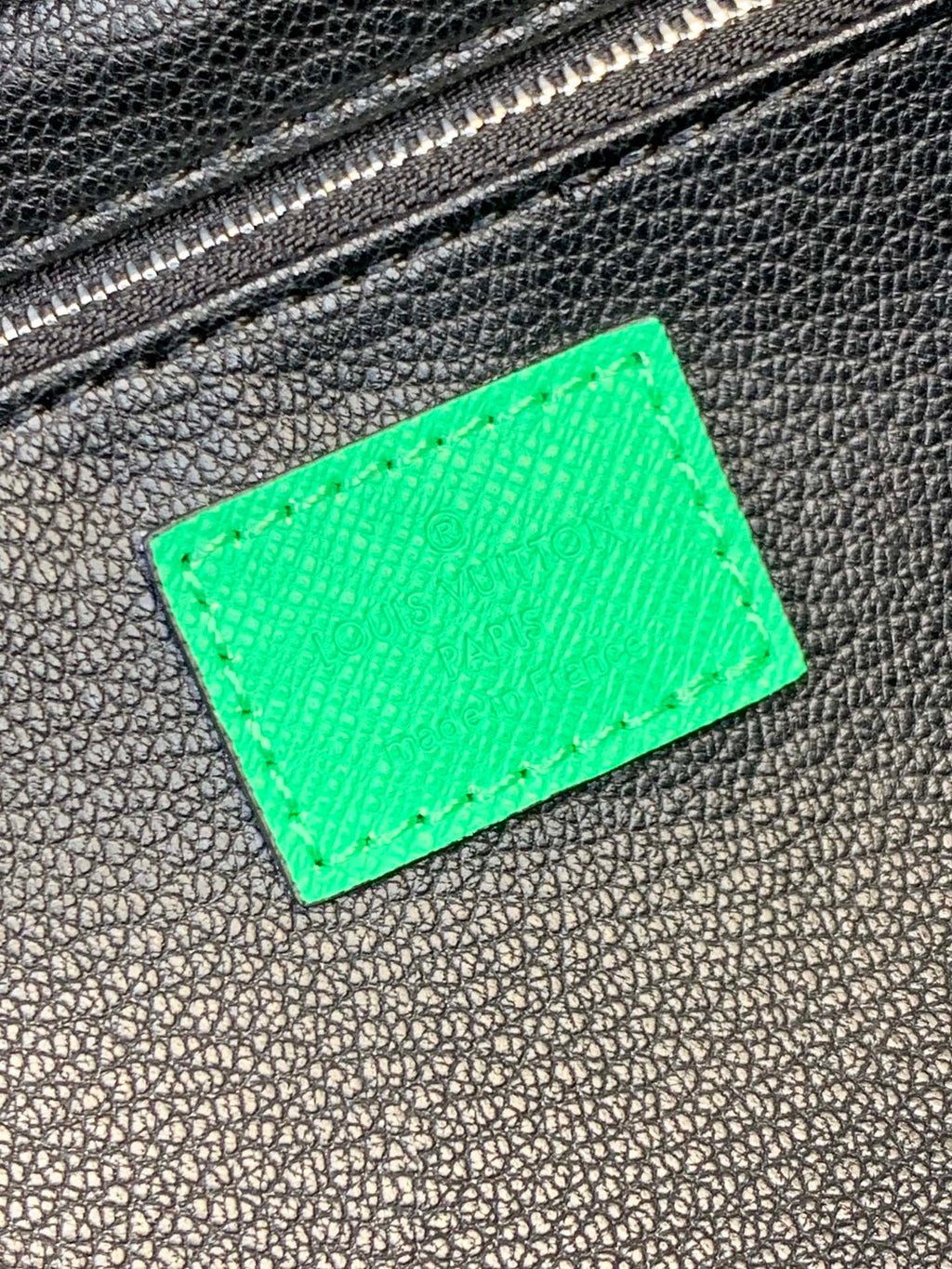 Green leather label patch on black textured bag with silver-tone zipper teeth
