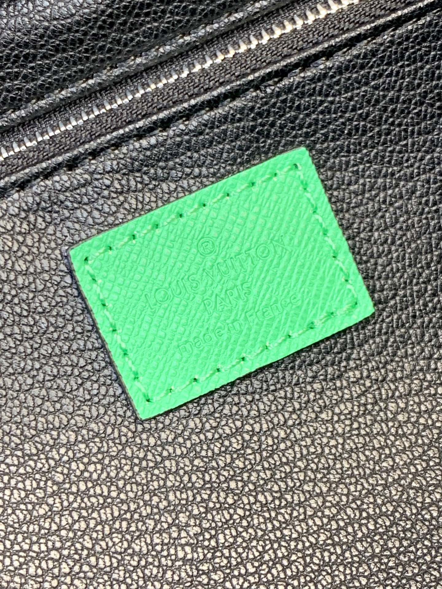 Green leather label patch on black textured bag with silver-tone zipper teeth