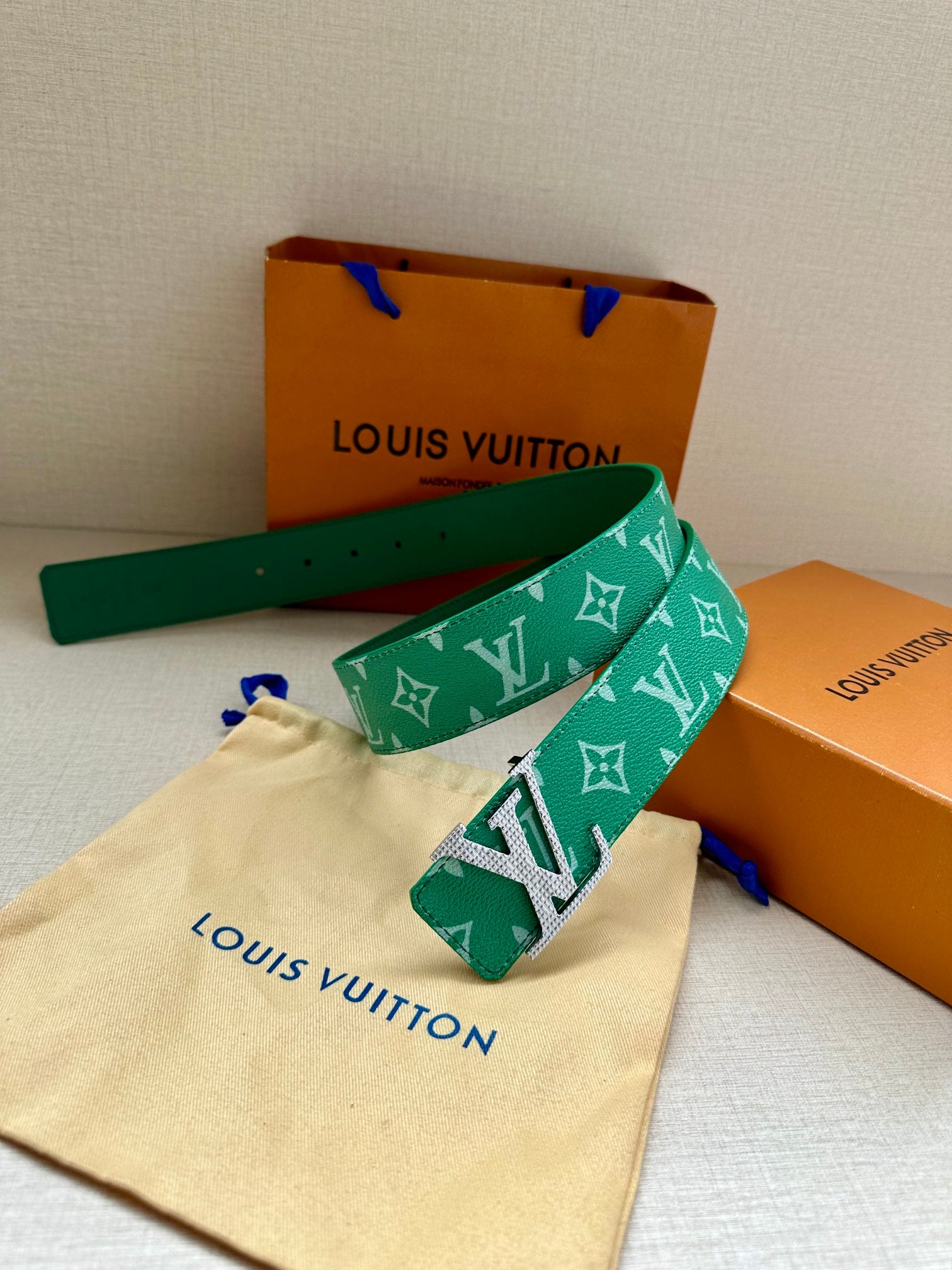Green logo belt with gold buckle and studded holes, with cream storage pouch