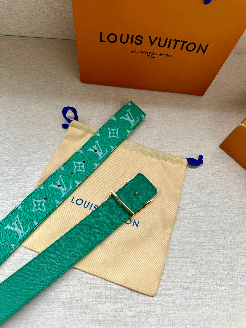 Green logo belt laid on cream dust bag with gold-tone buckle and small tag