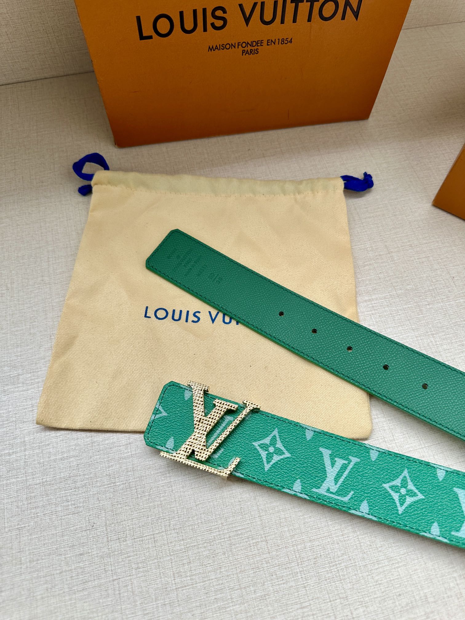 Green logo belt on cream dust bag with cutout keeper tab and holes