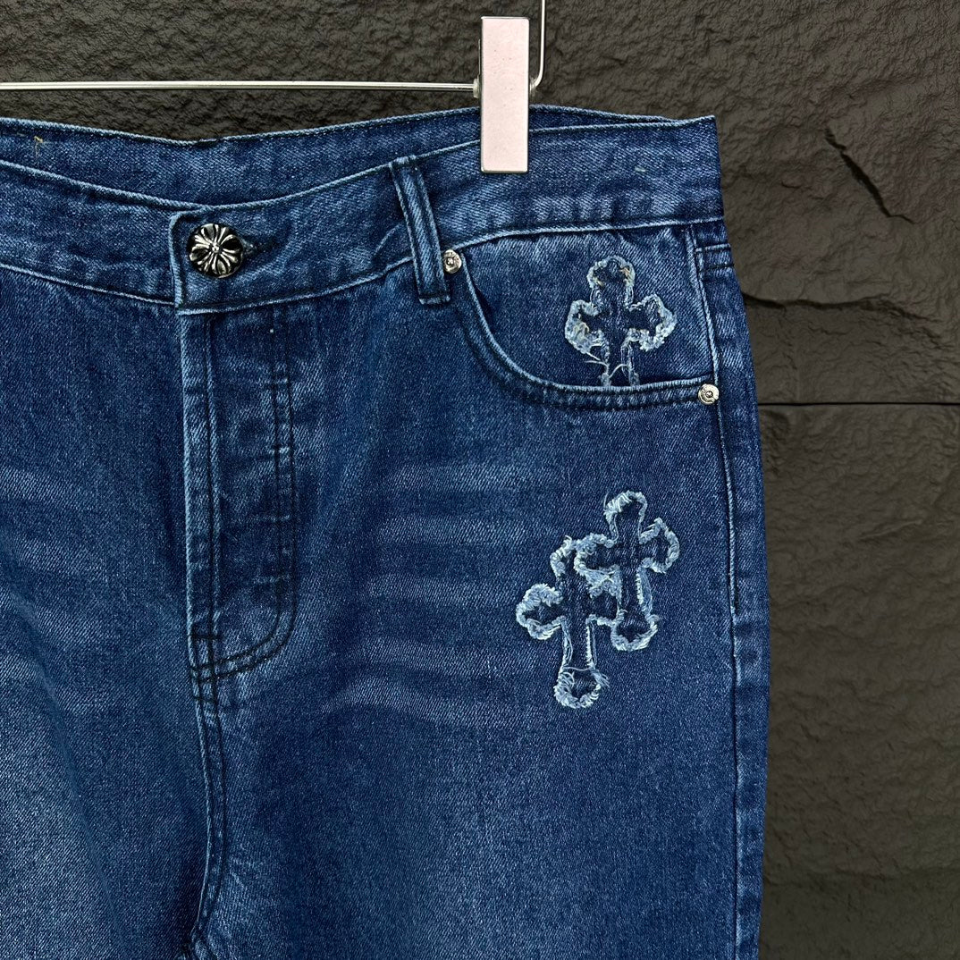 Blue denim pants close-up: waistband and front pocket with cross embroidery on denim.