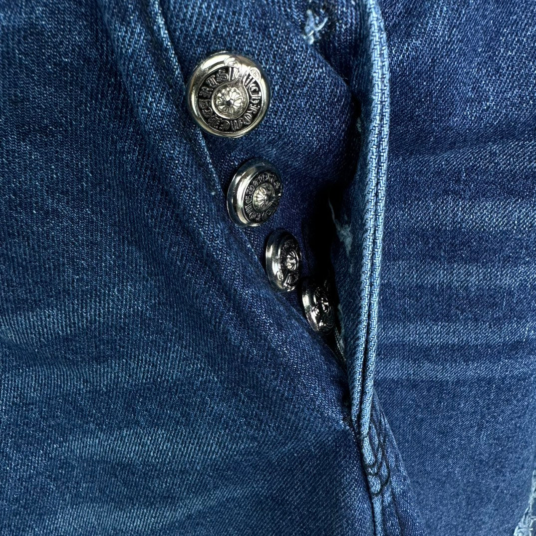 Blue denim pants close-up of button placket and zipper with stitched waistband seam.