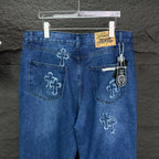 Blue denim pants back view with cross embroidery, rear pockets, and hanging charm tag.