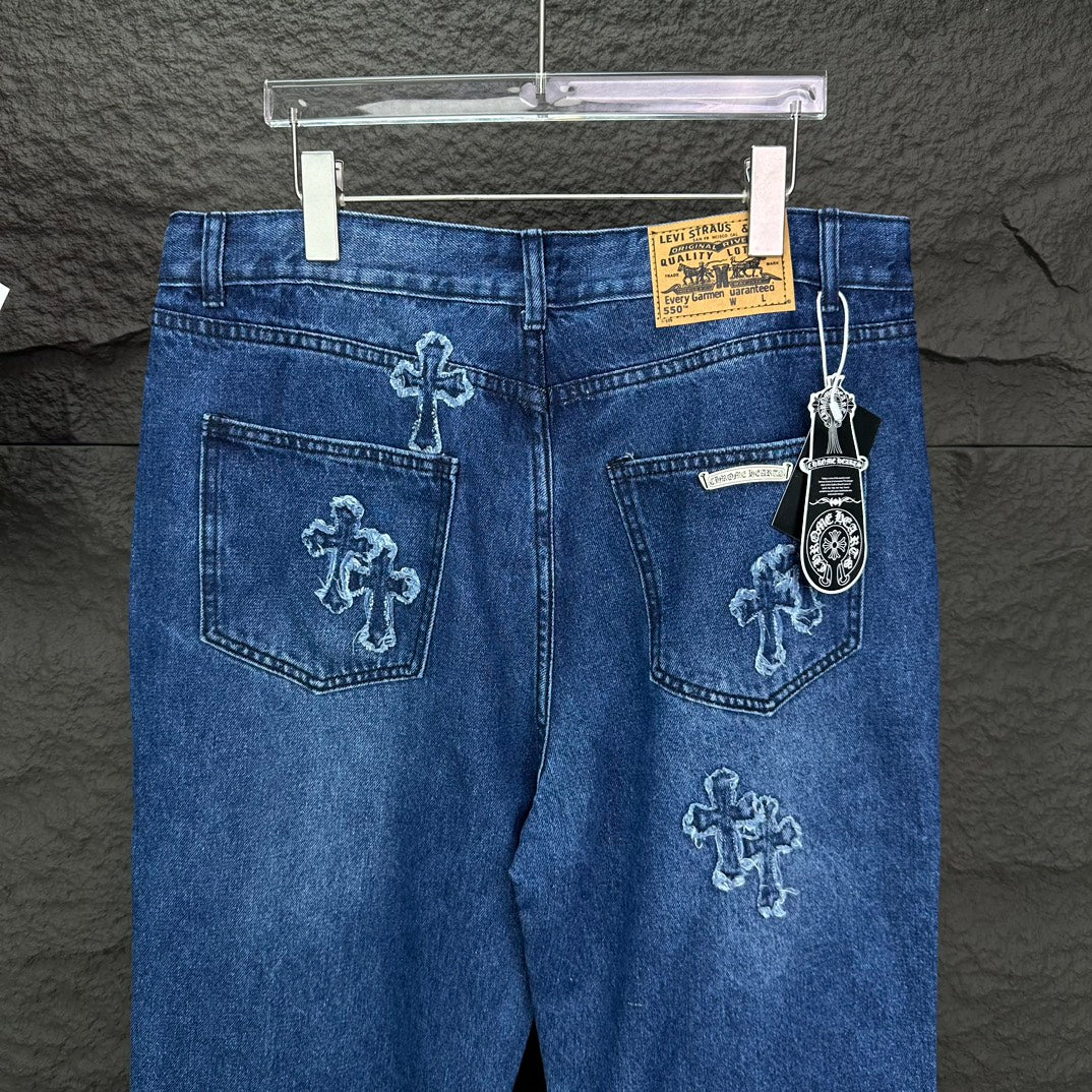 Blue denim pants back view with cross embroidery, rear pockets, and hanging charm tag.