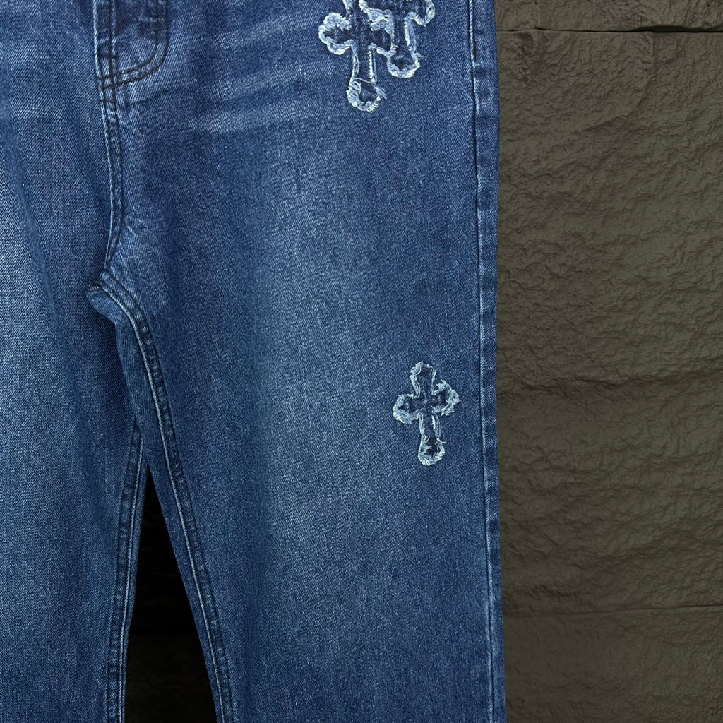 Blue denim pants side view with cross embroidery on leg near hem and inner seam.