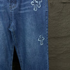 Blue denim pants side view with cross embroidery on leg near hem and inner seam.