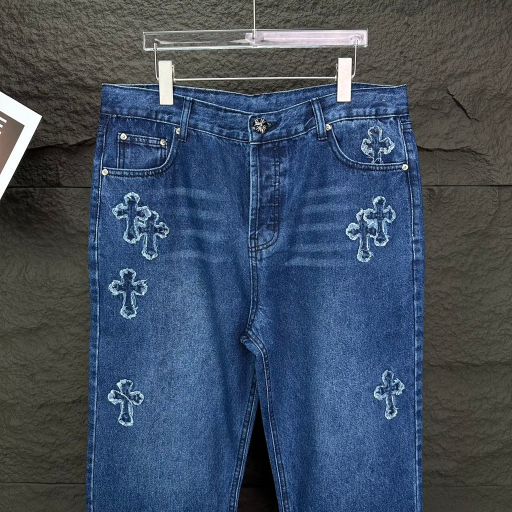 Blue denim pants front view with cross embroidery on legs and front pockets.