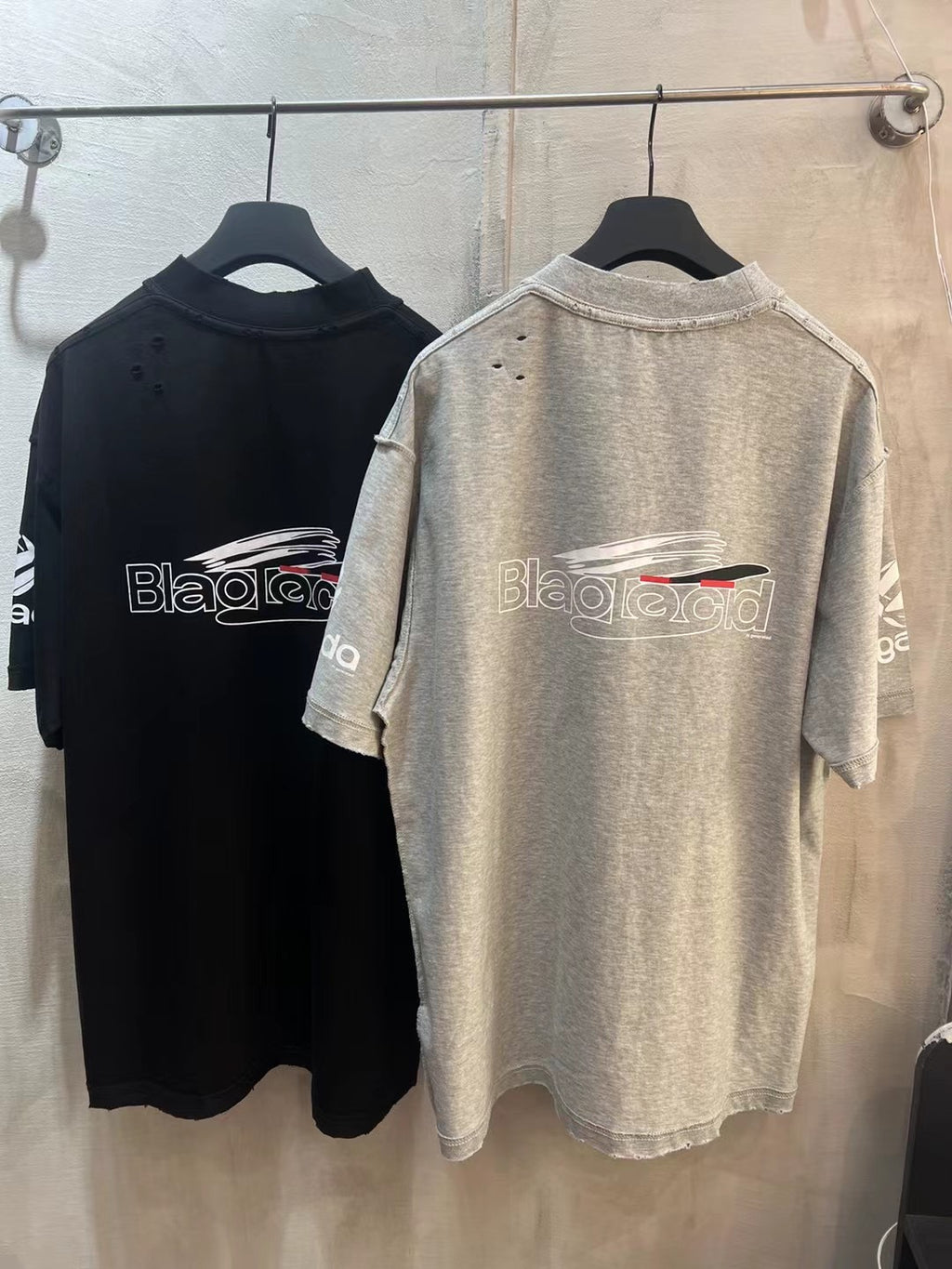 Two T-shirts on hangers: black and light gray with logo graphic