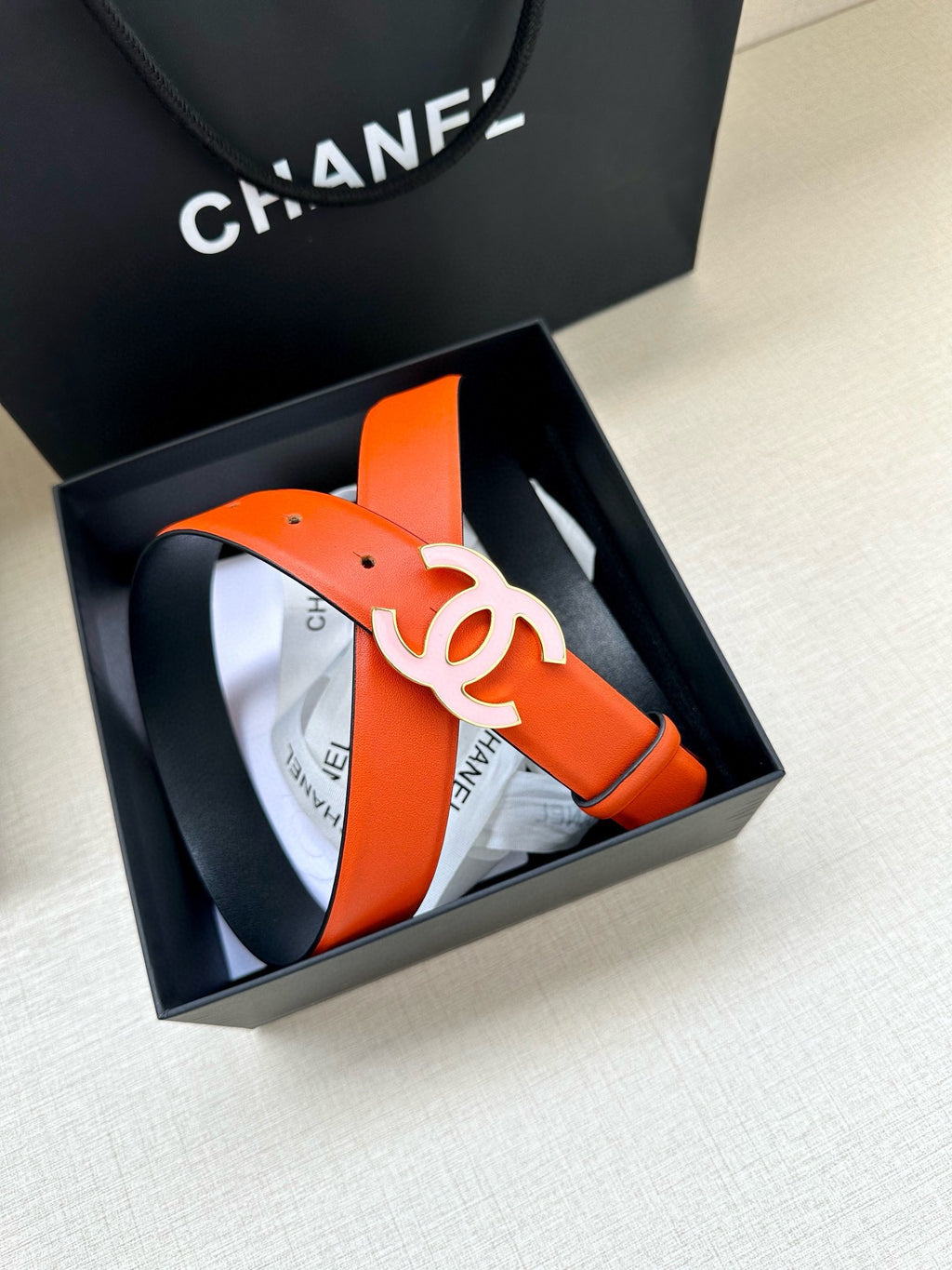 Chanel belt displayed in a box: bright orange leather strap with white CC buckle