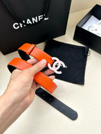 Chanel belt held by hand: bright orange leather strap with white CC buckle and holes