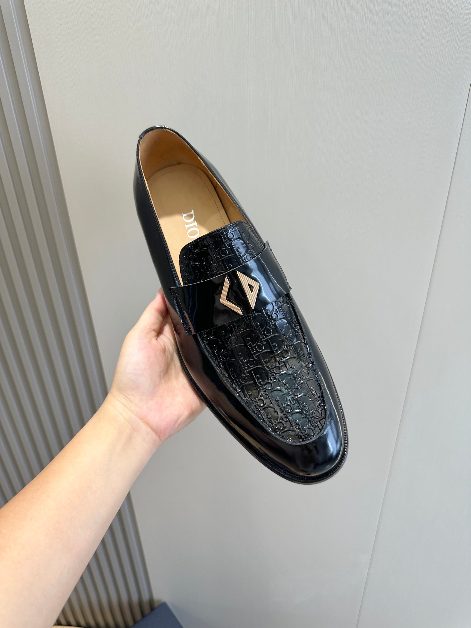 Dior unisex patent leather loafer, black with gold emblem, held in hand