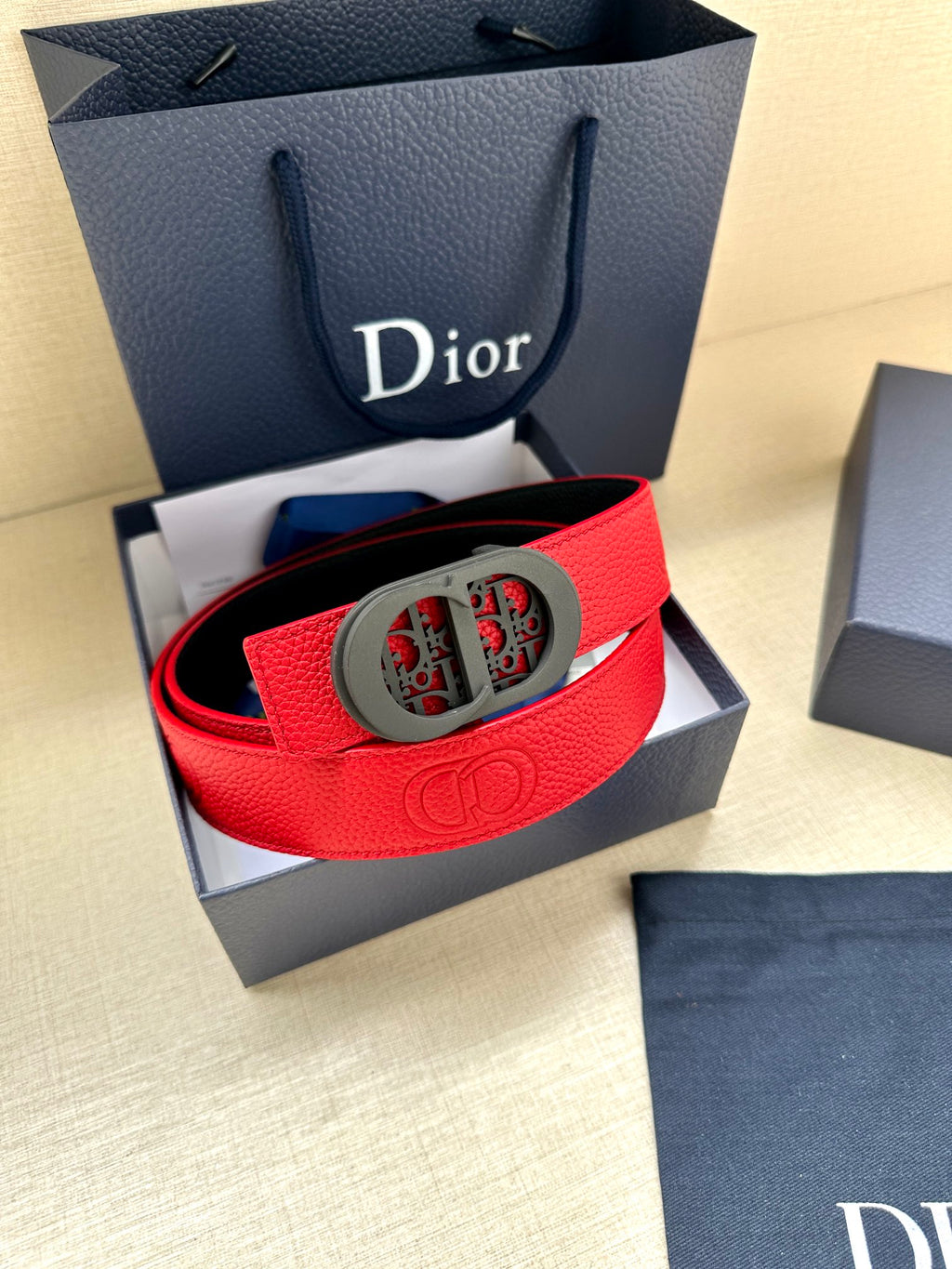Red Dior belt in leather with gray oval patterned buckle, shown in a gift box.