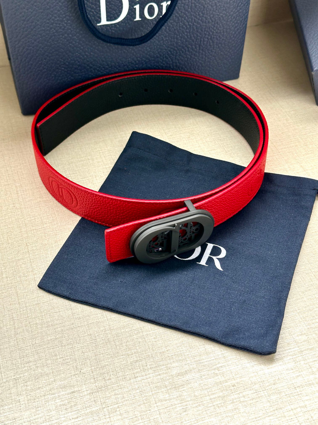 Red leather Dior belt with gray oval buckle and embossed detail on the strap.