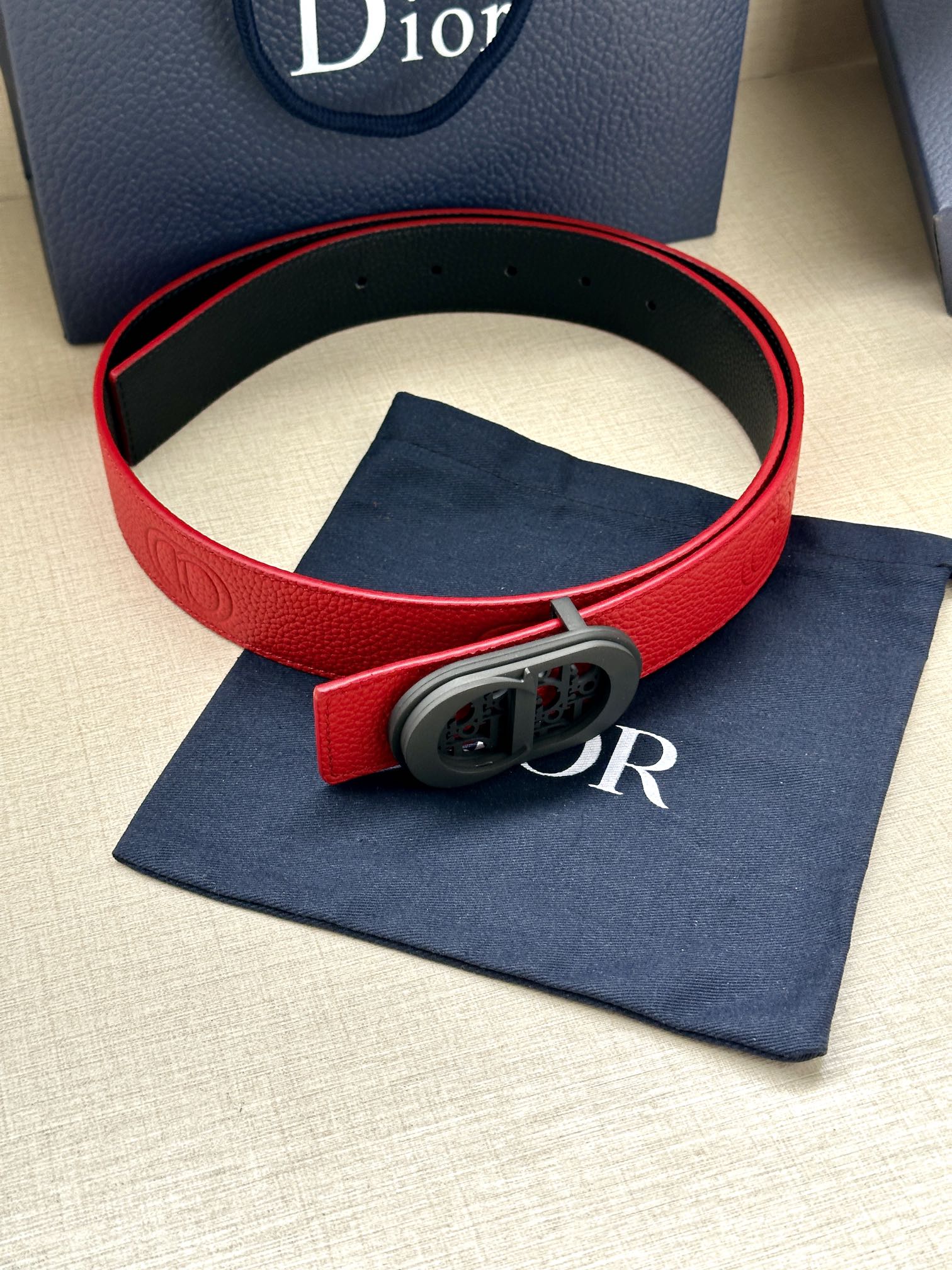 Red leather Dior belt with gray oval buckle and embossed detail on the strap.