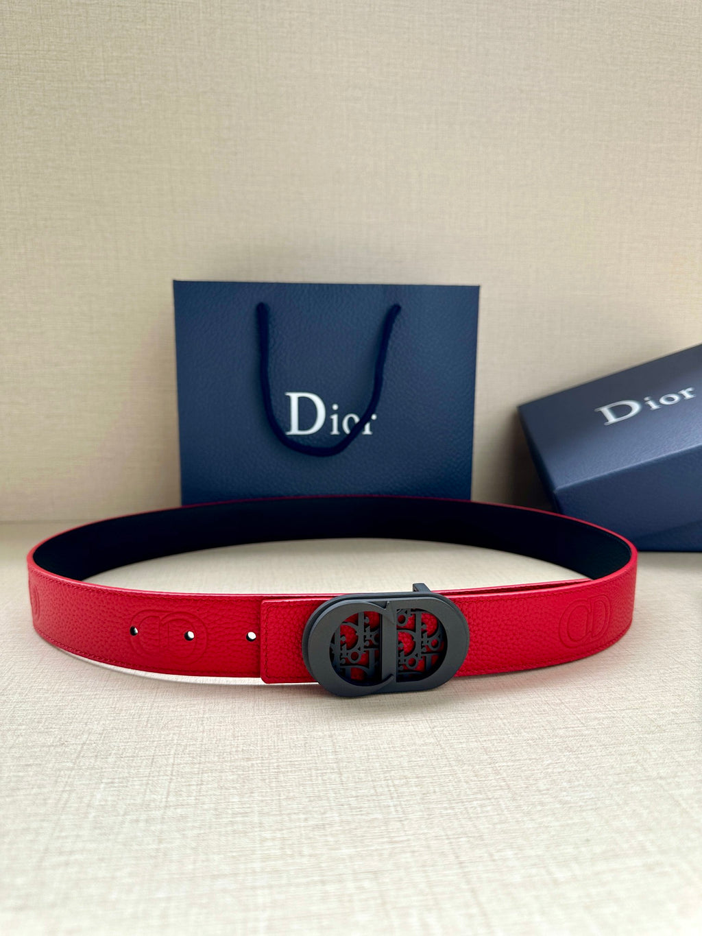 Dior belt in red leather with dark oval logo buckle and punched holes.